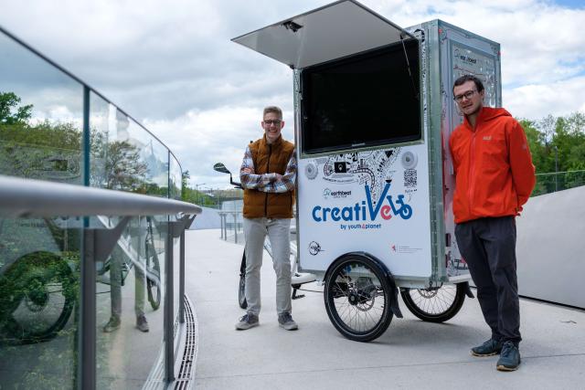 Deux jeunes hommes de l'assciation Youth4Climate, portraités sur un pont au Kirchberg avec leur vélo du projet Creativelo.