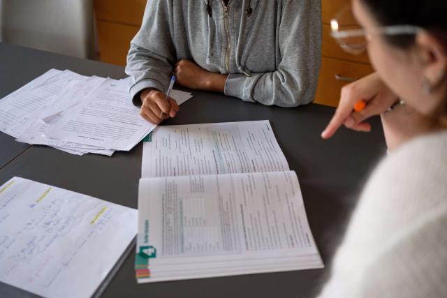 deux personnes en train d'étudier. On les voit assises sur une table sur laquelle se trouvent des feuilles et un livre.