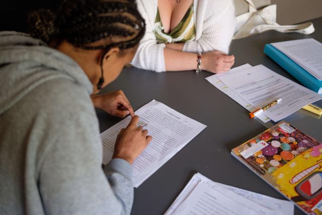 deux personnes en train d'étudier. On les voit assises sur une table sur laquelle se trouvent des feuilles et un livre.