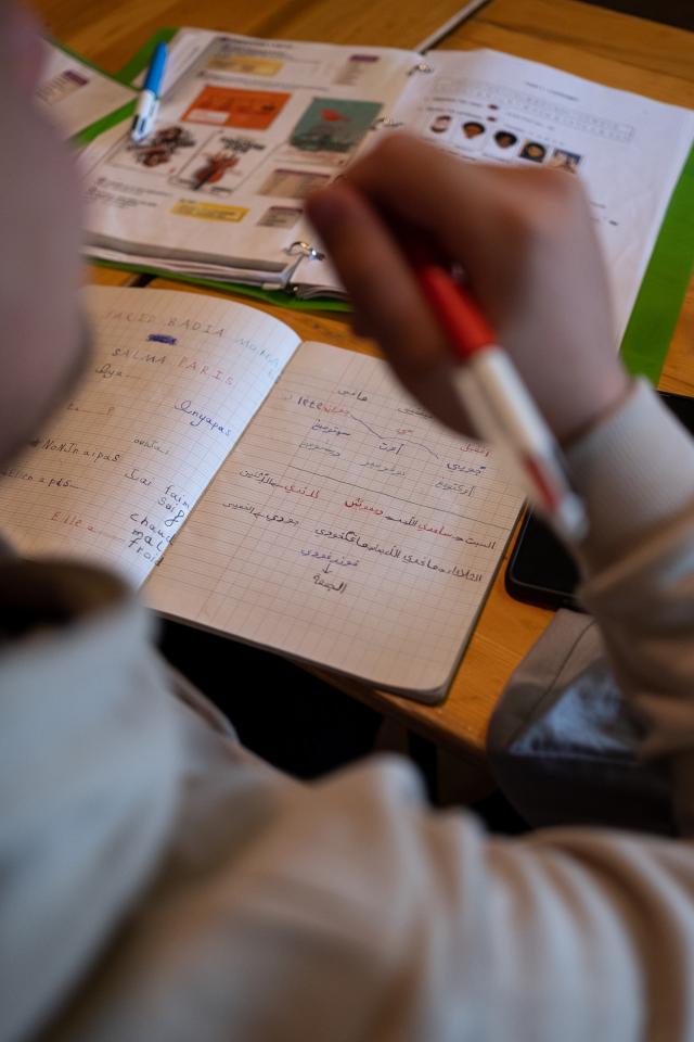 Schüler in einem Klassenzimmer, von hinten gesehen, mit offenen Lehrbüchern auf einem Tisch.