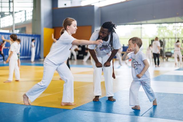 Un entraineur de Capoeira enseigne deux enfants dans un hall sportif