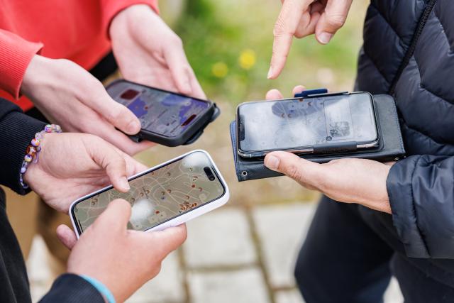 Photo des mains de 3 personnes qui tiennent tous leurs smartphone à la main pour regarder un plan de ville.