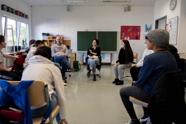 Schüler*innen und Lehrer*innen sitzen in einem Klassenzimmer