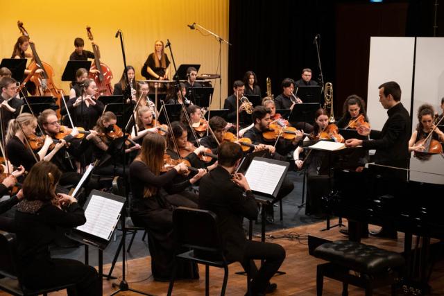 Musiker eines Orchesters auf einer Bühne, die in Gelb beleuchtet ist.