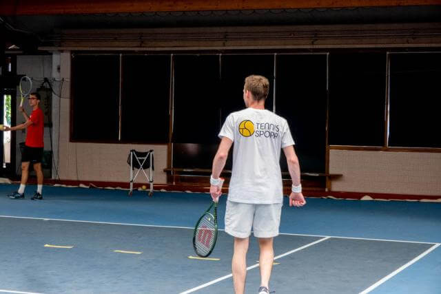 A man, his back to the camera, is holding a tennis racket in his hand